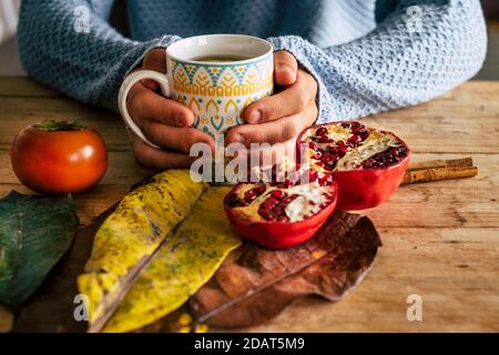 Primo piano della scena autunnale di casa indoor con Pair of le mani tengono una tazza di tè su un giallo di legno e tavola arancione con pompelmo e foglia Foto Stock