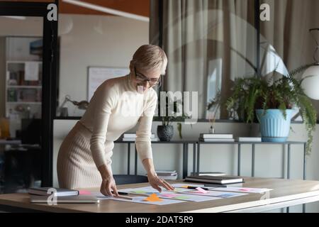 Donna d'affari sorridente e sicura che indossa occhiali che lavorano con documenti di progetto Foto Stock