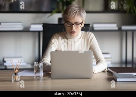 Donna d'affari sicura che indossa occhiali che lavorano su un computer portatile in ufficio Foto Stock
