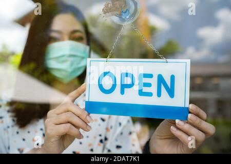 giovane donna proprietario con maschera viso aperto negozio dopo il blocco quarantena coronavirus (covid-19) pandemia Foto Stock