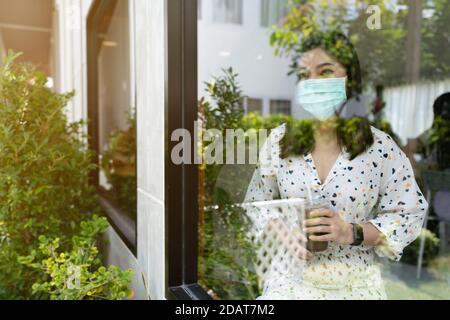 giovane donna che indossa una maschera per la protezione del coronavirus (covid-19) e. bere latte al cioccolato nel caffè Foto Stock