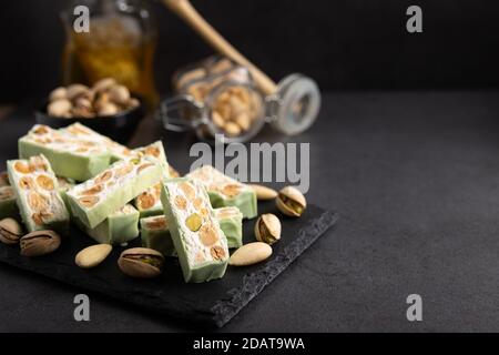 Torrone di organico a base di miele, pistacchi, nocciole, mandorle e i dadi su un rustico sfondo scuro. Foto Stock