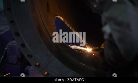 La smerigliatrice da lavoro taglia il metallo in fabbrica. Il lavoratore pesante dell'industria taglia un tubo enorme Foto Stock