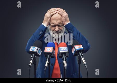 Triste politico con testa in mano al briefing dei media, si sente confuso e rammarico Foto Stock