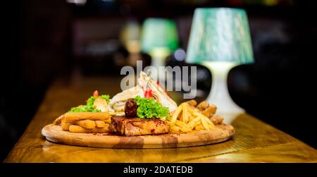 Pub menu snack. Ad alto contenuto calorico snack per il gruppo amici. Gustosi spuntini deliziosi. Snack per la birra. Il cibo del ristorante. Tavola di legno con un sacco di patatine fritte bastoncini di pesce burrito e bistecca di carne con insalata mista. Foto Stock