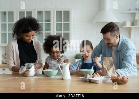 Felici genitori diversi con due figlie che cucinano pancake in cucina Foto Stock