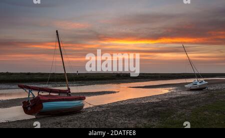 Due barche si siedono sul fango a bassa marea a Blakeney al tramonto. Foto Stock