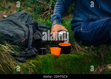 Bere tè da thermos durante l'escursione. Mano dell'uomo che versa il tè caldo dalla bottiglia nera del thermos. Rinfresco durante le escursioni Foto Stock
