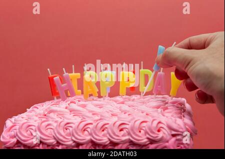 Primo piano di mano che mette la candela della torta sulla torta di compleanno con spazio di copia. Isolato su sfondo rosso. Foto Stock