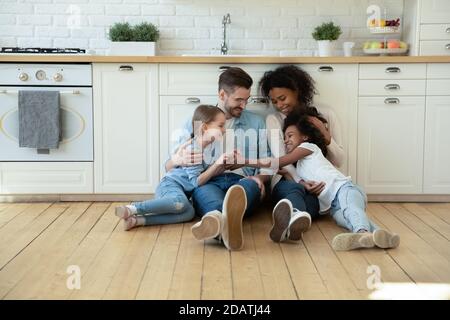 Felice famiglia multirazziale con bambini seduti a pavimento in cucina Foto Stock