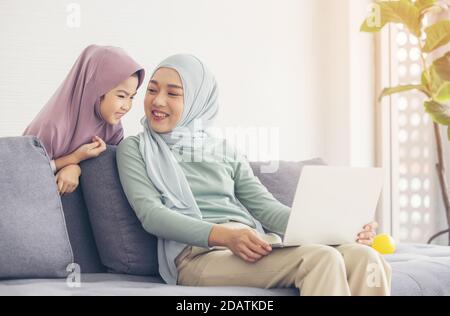 Madre musulmana asiatica e figlia sorridenti quando si usa il computer portatile insieme, navigare in Internet o guardare film in streaming Foto Stock