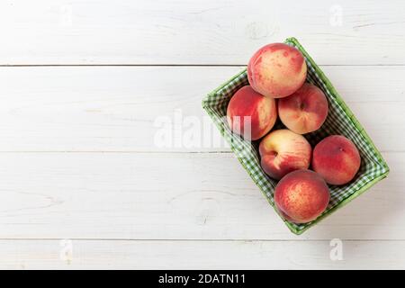 Pesche fresche e mature in un cestino su sfondo bianco di legno. Frutta deliziosa e sana. Concetto di cibo sano. Spazio per il testo. Vista dall'alto. Foto Stock