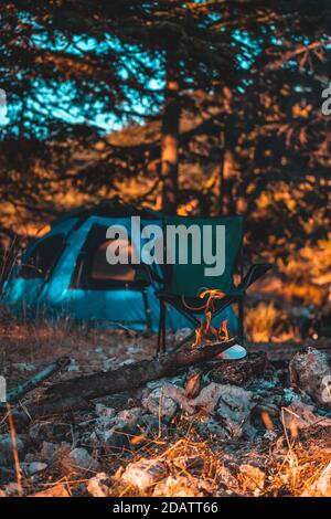 Tenda da campeggio, sedia portatile vicino al fuoco nella foresta. Nessuna gente. Luogo perfetto per un tranquillo riposo. Stile di vita attivo. Foto Stock