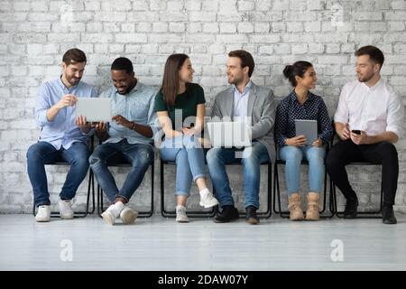 Persone diverse di generazione millenaria che parlano e utilizzano dispositivi elettronici Foto Stock