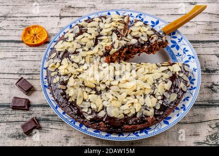 Torta di cacao e cocco ricoperta di glassa al cioccolato e scaglie di mandorle, con una fetta tagliata Foto Stock