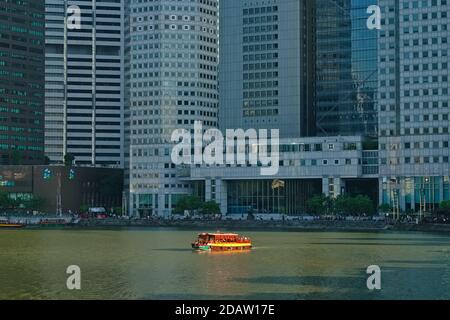 Un'escursione in barca illuminata dal sole sul Fiume Singapore a Singapore e' dwarfed dagli alti edifici del quartiere bancario di Raffles Place, Singapore Foto Stock