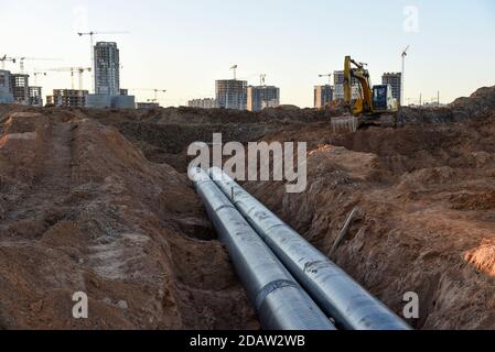 Escavatore durante la costruzione della conduttura principale di approvvigionamento idrico. Posa fognature sotterranee in cantiere. Acqua principale sistema di drenaggio sanitario Foto Stock