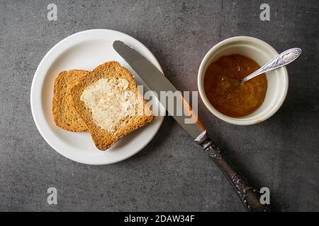 Tostare con burro su un piatto bianco con un coltello argentato. Sfondo grigio scuro con texture. Foto Stock