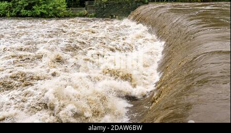 Acqua marrone fangosa in un fiume in piena dopo una tempesta che scorre veloce su una strana, con acque turbolente e pericolose sotto di essa. Foto Stock