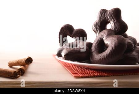 Biscotti al cioccolato a forma di cuore e stella su piatto bianco e bastoncini di cannella su tavolo di legno. Vista frontale. Composizione orizzontale. Foto Stock