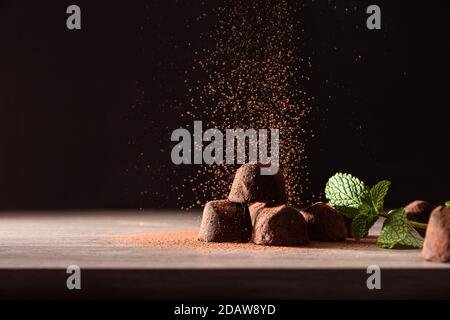 Tartufi di cioccolato con foglie di menta su tavola di legno e fondo scuro in polvere di cacao. Vista frontale. Composizione orizzontale. Foto Stock