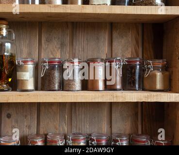 Bottiglie con spezie e condimenti in scaffale di legno. Varie erbe biologiche diverse per in cucina aspetto vintage Foto Stock