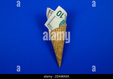 Primo piano gelato cialda di wafer cono con banconote in dollari americani arrotolate, sfondo blu Foto Stock