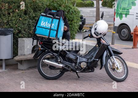 Atene, Grecia. 12 novembre 2020. Servizio di consegna del cibo Wolt, corriere seduto accanto allo scooter parcheggiato nella strada del centro della città Foto Stock