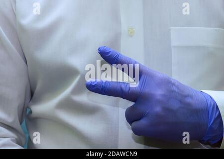 un uomo mostra due dita, forcelle - un gesto rude della mano in guanti di gomma medica monouso blu Foto Stock