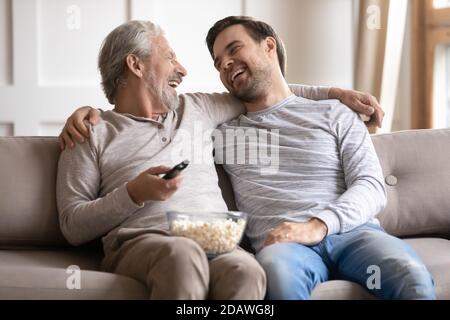 Felice padre più anziano con il figlio abbracciando, guardando la tv a casa Foto Stock