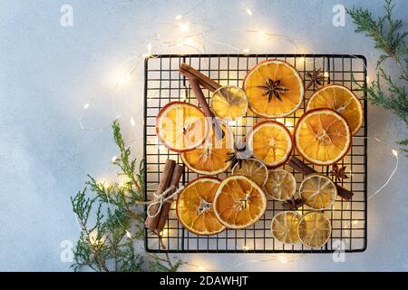 Arance secche, limoni, bastoni di cannella e stelle di anice su uno sfondo di luci di Natale e rami di abete. Foto Stock