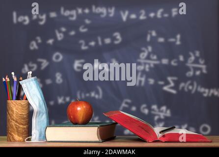 Concetto per il ritorno a scuola con coronavirus o Covid-19 con libri, mela e maschera viso contro la matematica sfondo lavagna per LA classe STEM Foto Stock
