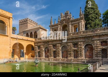 La Fontana con l'edificio storico con la pittura nel cortile dei palazzi Real Alcazar a Siviglia, Andalusia, Spagna Foto Stock