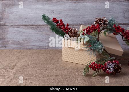 una carta fatta di una scatola regalo beige e di un Albero di Natale ramo con decorazioni su uno sfondo di legno e. burlap Foto Stock