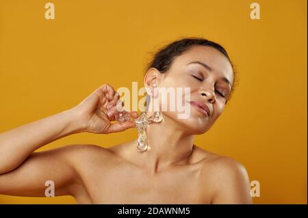 Ritratto della giovane donna africana su sfondo giallo, dandosi un massaggio del massaggiatore al collo faraone. Una donna con gli occhi chiusi, con Foto Stock