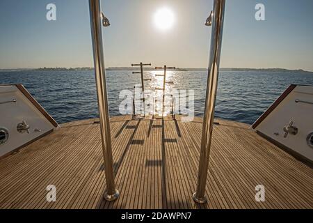 Scale in acciaio metallico sul ponte posteriore in legno di teak di a. grande yacht a motore di lusso che naviga su un oceano tropicale a. tramonto Foto Stock