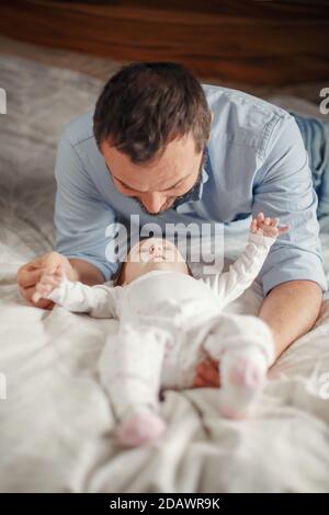 Giorno dei padri. Il padre caucasico gioca con la bambina appena nata a letto. Uomo genitore che parla con figlio di figlia. Autentico stile di vita felice padre di famiglia Foto Stock