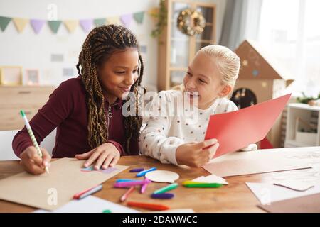 Ritratto di due ragazze adolescenti ridenti che si divertono a fare arte e a dipingere together mentre si siede alla scrivania nella sala giochi decorata Foto Stock