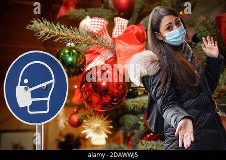 FOTOMONTAGE-Weihafterten 2020 nel mezzo della pandemia del coronavirus. E il blocco parziale? L'allentamento dei detenuti sarà probabilmente effettuato solo con un numero di corona significativamente decrescente. Giovane donna con maschera facciale, mascherine in piedi perplessi davanti a Weihaftertsbaum, Weihafterten, albero di Natale, albero di Natale, albero di Natale, decorato, palla albero di Natale. | utilizzo in tutto il mondo Foto Stock