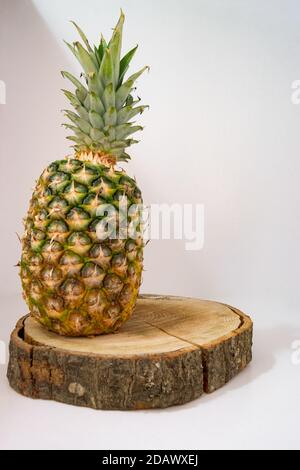 Ananas fresco intero poggiato su un ceppo di legno con un sfondo bianco e un raggio di luce Foto Stock
