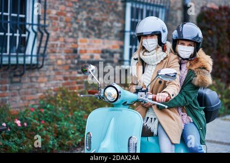 Due donne che indossano maschere e si spostano su scooter Foto Stock