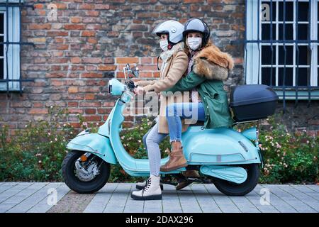 Due donne che indossano maschere e si spostano su scooter Foto Stock