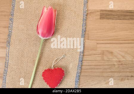 Colpo di testa di un tulipano rosso e cuore fatto a mano contro il panno di tela di tela su tavolo di legno Foto Stock