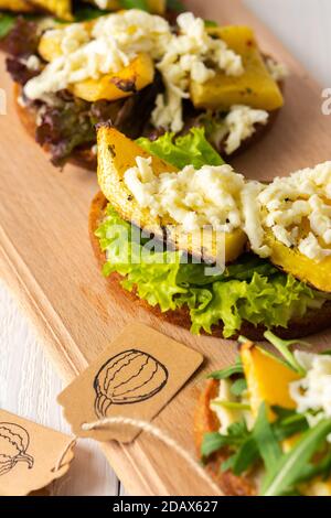 Panini tostati con formaggio brie, zucca al forno e insalata, rucola e mozzarella, deliziosi spuntini vegetali su tavola di legno Foto Stock