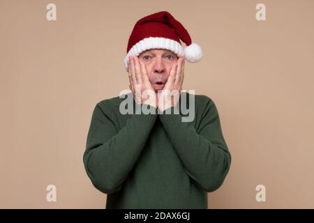 L'uomo ispanico sorpreso che indossa cappello rosso di natale che è scioccato. Foto Stock