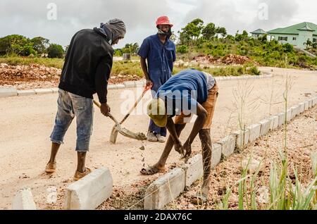 Tre uomini al lavoro su un cantiere stradale. Mentre una si piega per stendere blocchi di calcestruzzo, l'altra fornisce morde umide per la posa dei blocchi, Foto Stock