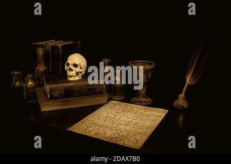 Antica scrivania spooky in seppia, con pergamena, penna di piume, calice, libri, cranio e bottiglie. Pergamena è rune arcane. Atmosfera antica di seppia. Foto Stock