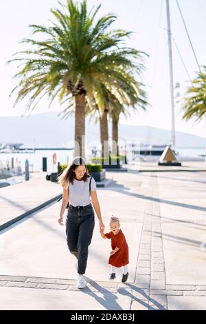 Mamma e figlia corrono e si divertono su un molo delle barche vicino al mare Foto Stock