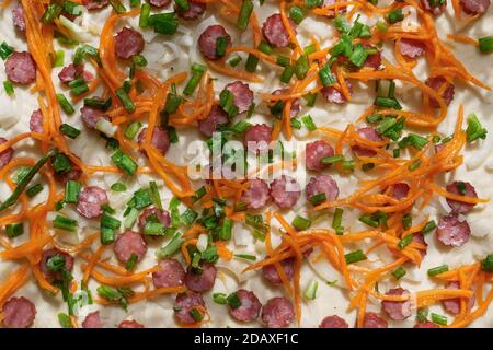 Dettaglio della pizza durante la preparazione alla cottura con ingredienti di salsicce, carote a fette lunghe, foglie di cipolla verde e senza altra componente Foto Stock