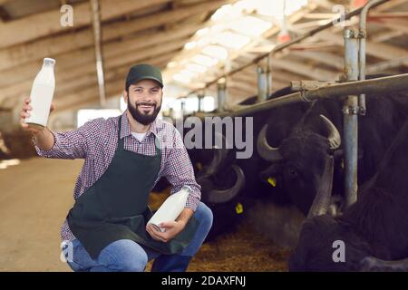 Contadino felice mostrando bottiglie di fresco latte di bufalo naturale prodotto sulla sua fattoria Foto Stock